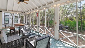 A covered outdoor area with wicker furniture, a ceiling fan, and large windows overlooking a garden. - 30A Beach Bungalow in Inlet: Steps from Sea, Pool with Golf Cart & Cruiser Bikes (Seacrest)
