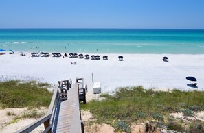 A beach with a wooden boardwalk leading to the shore, clear turquoise water, and beach umbrellas.