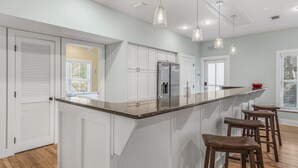 A modern kitchen with white cabinets, a stainless steel refrigerator, and a bar area with stools. - 30A Beach Bungalow in Inlet: Steps from Sea, Pool with Golf Cart & Cruiser Bikes (Seacrest)