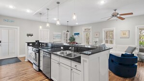 A modern kitchen with white cabinetry, a black countertop, stainless steel appliances, pendant lighting, and a ceiling fan. - 30A Beach Bungalow in Inlet: Steps from Sea, Pool with Golf Cart & Cruiser Bikes (Seacrest)