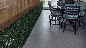 A covered patio area with a table and chairs, a wall with a textured surface, and a green hedge. - Cozy 55+ Punta Gorda Home - Pet Friendly, Fully Furnished! Pool/Lake/Club (Punta gorda)