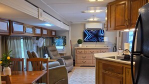 A compact RV interior with a dining area, seating, a kitchenette, and a TV. - Cozy 55+ Punta Gorda Home - Pet Friendly, Fully Furnished! Pool/Lake/Club (Punta gorda)