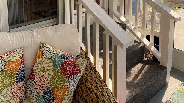 A covered porch with a white railing, a wicker bench, and colorful cushions. - Cozy 55+ Punta Gorda Home - Pet Friendly, Fully Furnished! Pool/Lake/Club (Punta gorda)