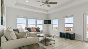 A spacious living room with a sofa, coffee table, and a TV mounted on the wall. - Pelican Shores: Sun, Sand, and Serenity – 3BR Beachfront Retreat! (Gilchrist)