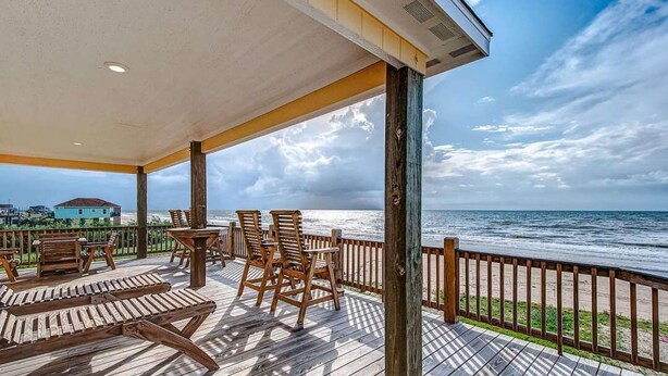 A wooden deck with chairs and a table overlooking the ocean. - Pelican Shores: Sun, Sand, and Serenity – 3BR Beachfront Retreat! (Gilchrist)