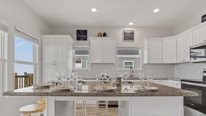 A modern kitchen with white cabinets, a granite countertop, and bar stools. - Pelican Shores: Sun, Sand, and Serenity – 3BR Beachfront Retreat! (Gilchrist)