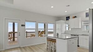 A spacious kitchen with a large island, white cabinetry, and a view of the beach through the sliding glass doors. - Pelican Shores: Sun, Sand, and Serenity – 3BR Beachfront Retreat! (Gilchrist)