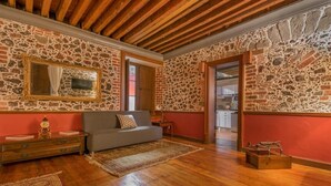 A room with stone walls, a wooden ceiling, a sofa, a mirror, and a wooden floor. - Casa Sauto (Mexico City)