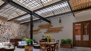 A spacious patio area with a stone wall, wooden furniture, and a table with sunflowers. - Casa Sauto (Mexico City)