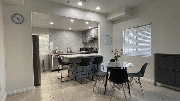 A modern kitchen with a central island, bar stools, and a dining table with chairs.