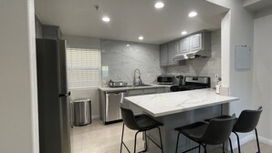 A modern kitchen with a large island, stainless steel appliances, and black bar stools.