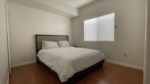 A bedroom with a bed, a nightstand, and a window with blinds.