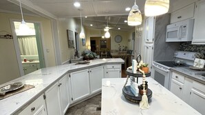 A modern kitchen with white cabinetry, a marble island, pendant lighting, and a microwave. - Redecorated 3 Bed ,2 Bath ,Sofa bed Outdoor shower Come relax at our beach house (Surfside Beach)
