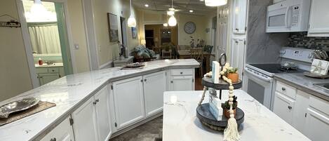 A modern kitchen with white cabinetry, a marble island, pendant lighting, and a microwave.