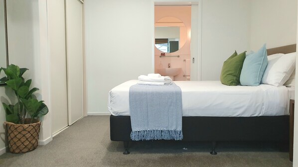 A bedroom with a bed, a potted plant, and a bathroom visible through an open door. - City Living - Wifi- Netflix - Laundry (Auckland)