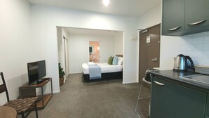 A compact hotel room with a bed, a small desk with a TV, a kitchenette, and a bathroom visible through an open door. - City Living - Wifi- Netflix - Laundry (Auckland)