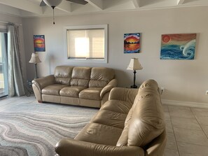 A living room with a beige sofa, two armchairs, a patterned rug, and three paintings on the wall. - Beautiful Melbourne Beach Oceanfront Townhouse (Melbourne Beach)