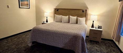 A hotel room with a large bed, two bedside tables with lamps, a headboard, and a framed picture on the wall.