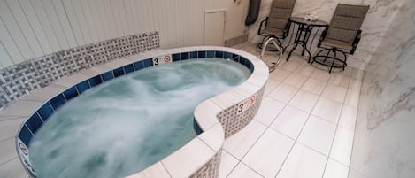 Et spabad med skilt, der angiver en dybdebegrænsning på 90 centimeter, omgivet af flisegulv og et siddeområde med stole og et bord.