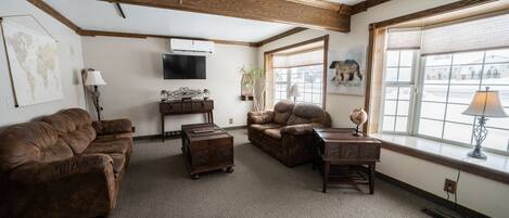 A living room with two brown leather sofas, a wooden coffee table, and a small side table with a lamp. There is a world map on the wall and a painting of a dog.