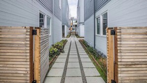 A narrow pathway flanked by wooden fences leading to a row of modern buildings with large windows.