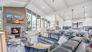 A spacious living room with a fireplace, a large sofa, and a dining area with a kitchen in the background. - Breathtaking Views, Ideal Location, Peaceful Lounging Area (Sedona)