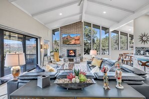 A spacious living room with a fireplace, comfortable seating, and large windows offering views of the outdoors.