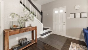 A modern hallway with a wooden console table, a staircase, and a door with framed notes. - •The Gem•Arcade•Covered Parking•Pets•Central! (Euless)