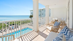 Ein Balkon mit Pool, weißen Möbeln und Blick aufs Meer.