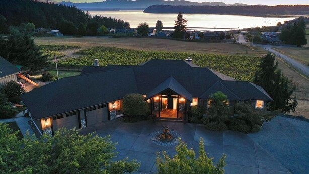 A large house with a dark roof, a driveway, and a landscaped front yard with a fountain.