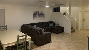 A living room with a sectional sofa, a dining table with chairs, a ceiling fan, and a staircase leading to another level. - Fun 4 bedroom house w/ splash pad, near City Center and Saguaro National Forest (Tucson)