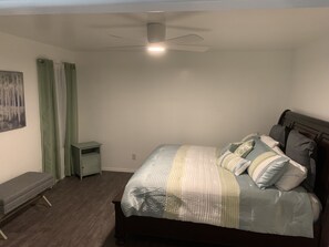 Ein Schlafzimmer mit einem Bett, einem Nachttisch, einer Bank, einem Deckenventilator und einem Bild an der Wand.