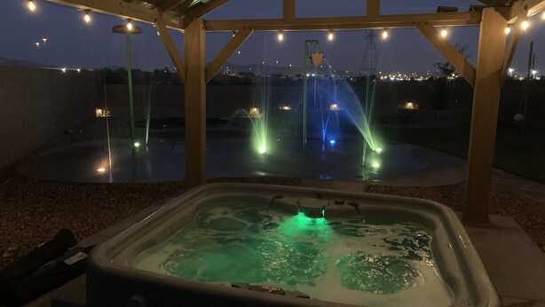 A hot tub under a wooden pergola with string lights, surrounded by a water feature with fountains. - Fun 4 bedroom house w/ splash pad, near City Center and Saguaro National Forest (Tucson)