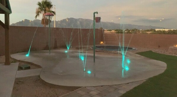 Ein Wasserspiel mit mehreren Wasserstrahlen, einem kreisförmigen Pool und einer Palme.