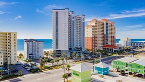 A coastal hotel area with multiple high-rise buildings, a parking lot, and a beach in the background. - Seawind 1005 | Beautiful condo with perfect beach view and walk to dine, shop, more! (Gulf Shores)