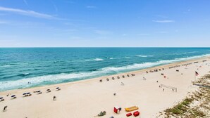 A beach with a volleyball net, umbrellas, and a flag. - Seawind 1005 | Beautiful condo with perfect beach view and walk to dine, shop, more! (Gulf Shores)