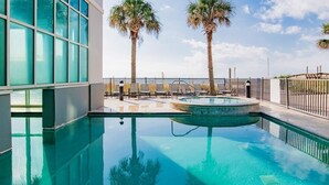A swimming pool with two palm trees, a fenced deck, and a modern building with large windows. - Seawind 1005 | Beautiful condo with perfect beach view and walk to dine, shop, more! (Gulf Shores)
