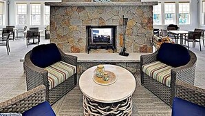 A spacious living area with a stone fireplace, wicker furniture, and a view of the dining area. - Sunkissed cottage, heated pools, club house, game room, 15 mins to local beaches (Arundel)