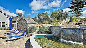 A pool area with lounge chairs and a stone wall. - Sunkissed cottage, heated pools, club house, game room, 15 mins to local beaches (Arundel)
