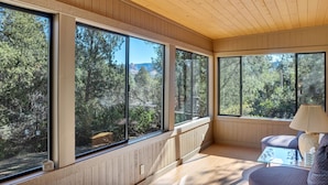 A room with large windows, wooden ceiling, and a small table with a lamp.