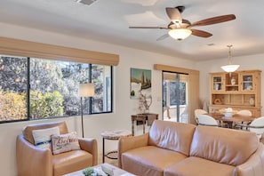 Relax in this inviting living room with a sofa, armchair, and dining area, offering a view of the surrounding trees and foliage.