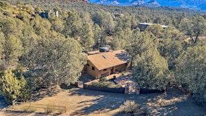 A house surrounded by dense forest with a clear view of red rock formations in the background.