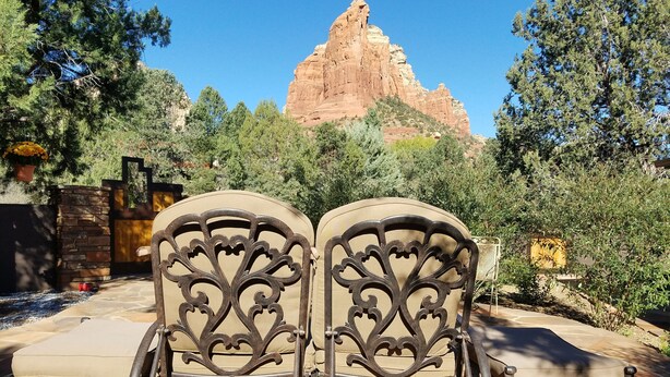 Two outdoor lounge chairs with ornate metal backrests, positioned on a patio with a view of a large red rock formation in the background.