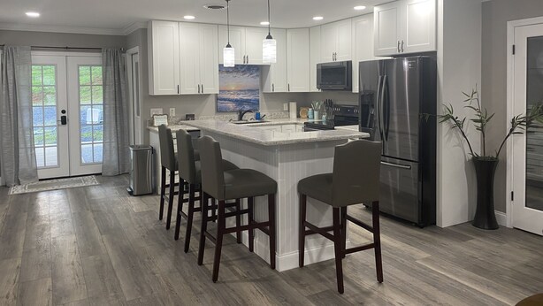 Una cocina moderna con armarios blancos, un refrigerador de acero inoxidable, un microondas y una isla grande con taburetes de bar.