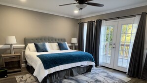 Un dormitorio con cama, ventilador de techo, mesita de noche, lámpara y vistas a través de una puerta.