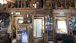 A rustic cabin interior with wooden beams, a loft area, and a cabin sign.