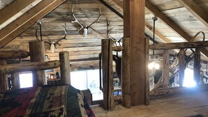 A rustic interior with wooden beams, a high ceiling, and antlers hanging from the beams.