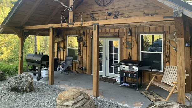 A rustic cabin with a covered porch, a grill, and a large rock in the foreground.
