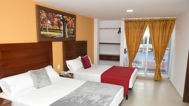 A hotel room with two beds, a wooden headboard, a painting, a window with curtains, and a balcony view. - Hotel Kai Soledad (Soledad)