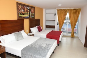 Habitación de hotel con dos camas, cabecero de madera, un cuadro, ventana con cortinas y vistas al balcón.